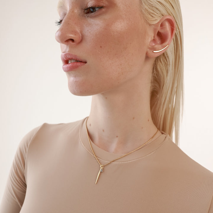 The Needle Solitaire Necklace, which is a single gold necklace, features a sleek needle-shaped pendant with a sparkling solitaire crystal accent. This elegant and minimalistic piece is perfect for standalone wear or layering with other gold necklaces for a sophisticated style