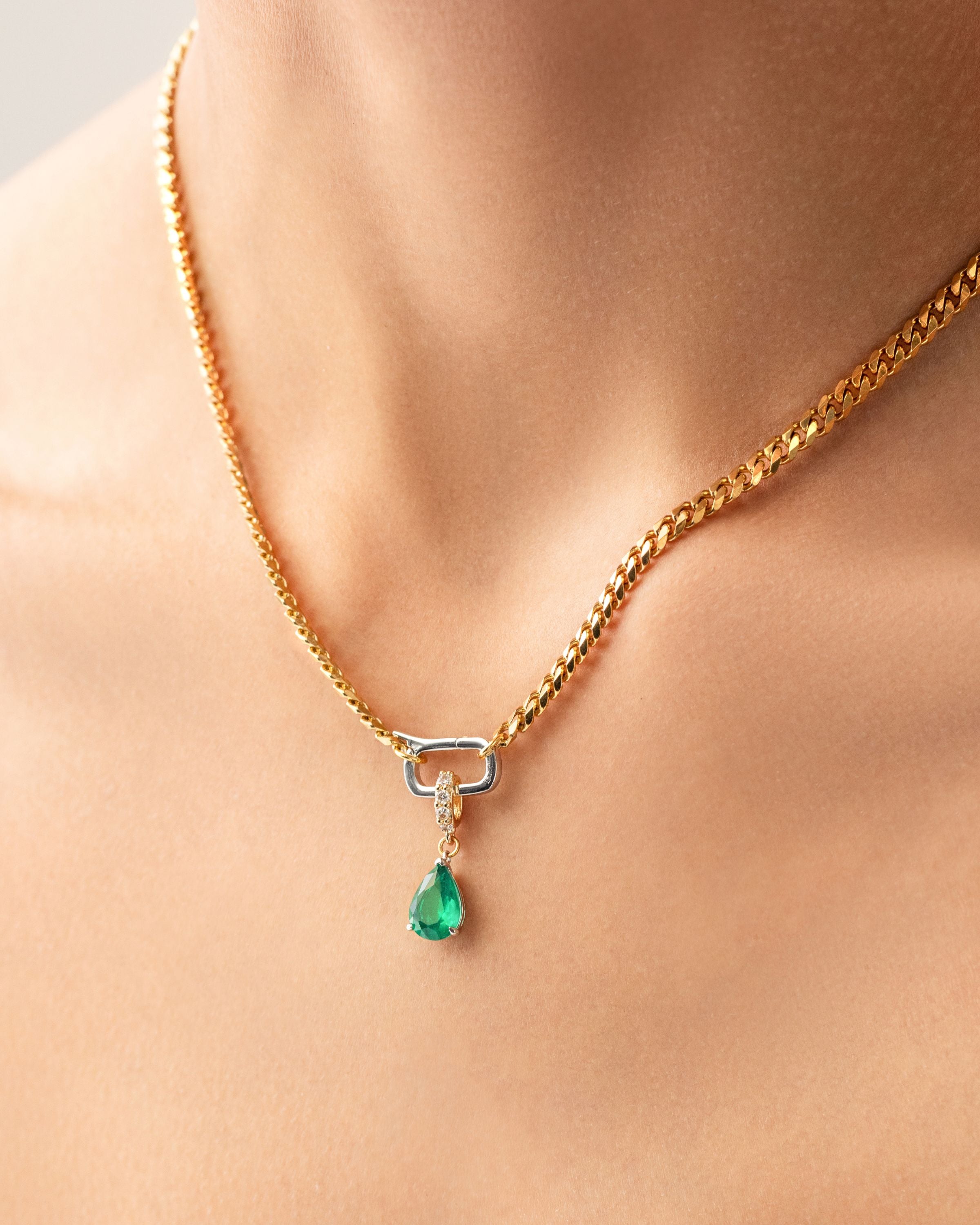 Model wearing a gold necklace with can opener clasp with the Emerald Teardrop Clip On Charm, a gold charm featuring a single teardrop-shaped emerald. ||| GOLD