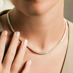 The Gold Tennis Necklace, a single gold necklace elegantly draped along the neckline, featuring a continuous row of sparkling round crystals. This timeless piece adds a sophisticated shimmer, perfect for both everyday elegance and special occasions.