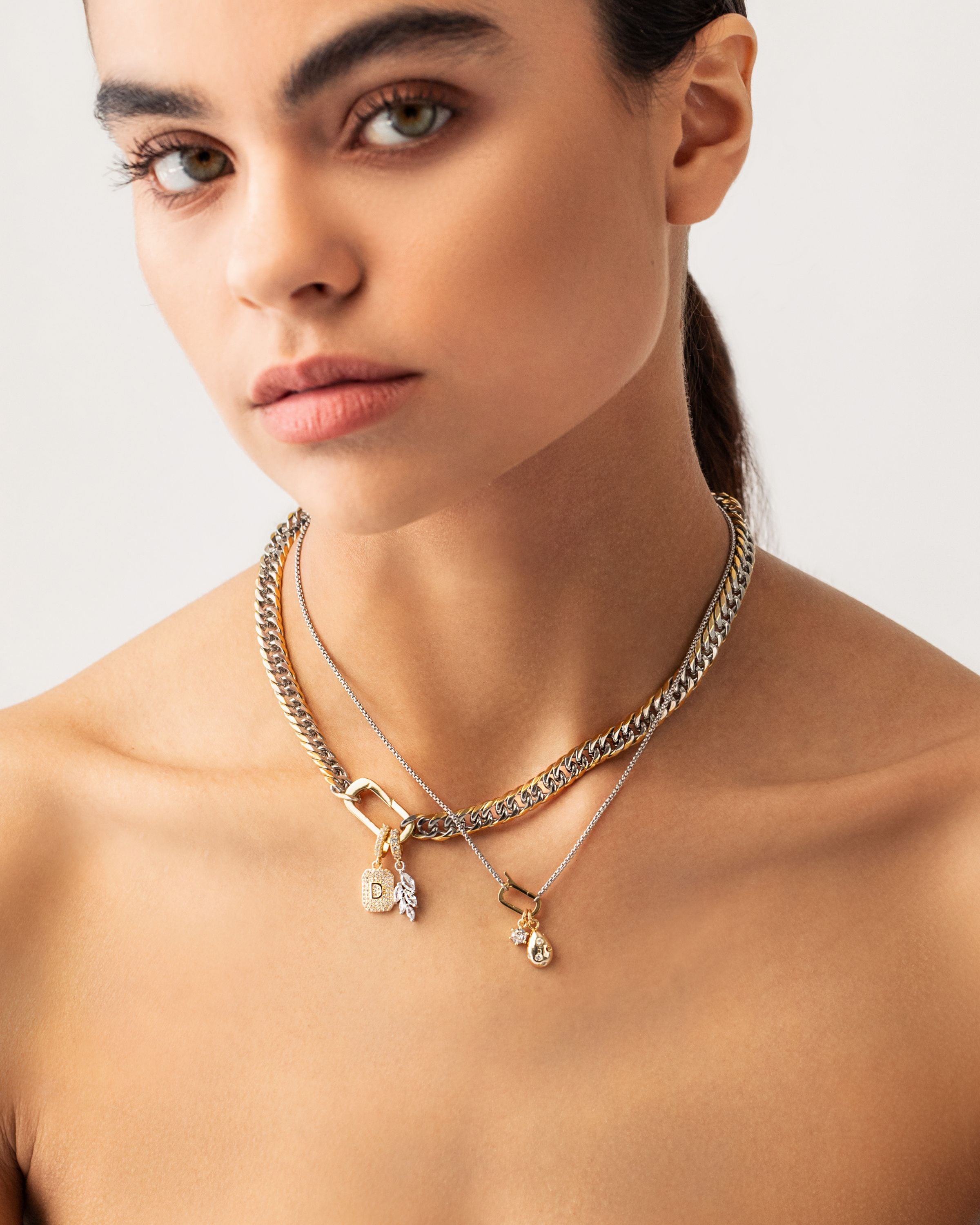 Model wearing the JUST CLICK CHARM PARTY NECKLACE SET showcasing mixed metal chains in gold and silver, adorned with delicate charms, including a lock, teardrop pendant, and crystal accents, elegantly styled on a model's neck.