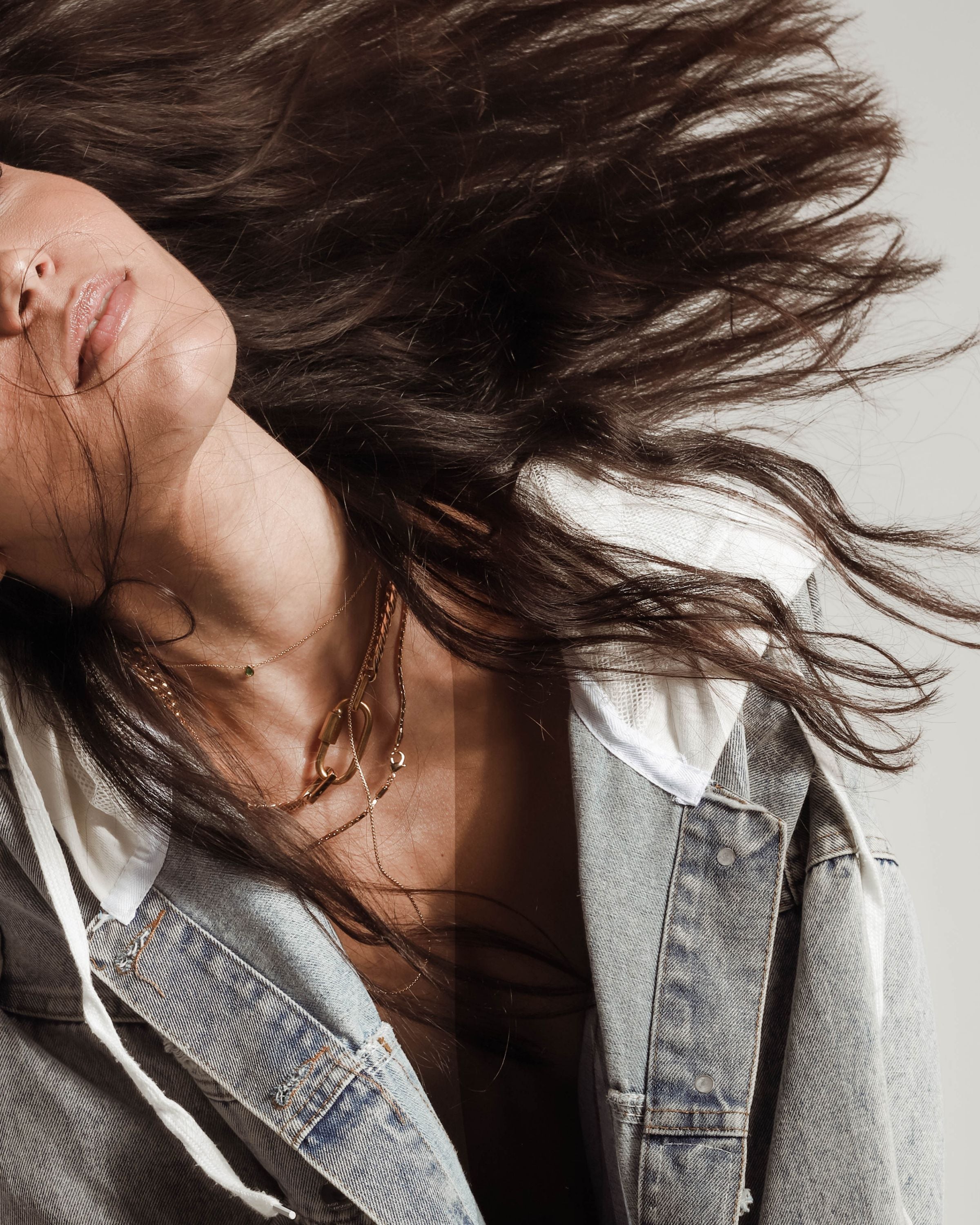 Model wearing an oversized denim jacket and The ANNE GOLD NECKLACE SET which includes 4 separate layered chains. The shortest is the Anne Necklace made of chunky 18k gold plated stainless steel chain with carabiner clasp followed with two thin necklaces that are 20" and 24" in length and a necklace with 925 Sterling Silver Gold plated emerald drop dainty charm.