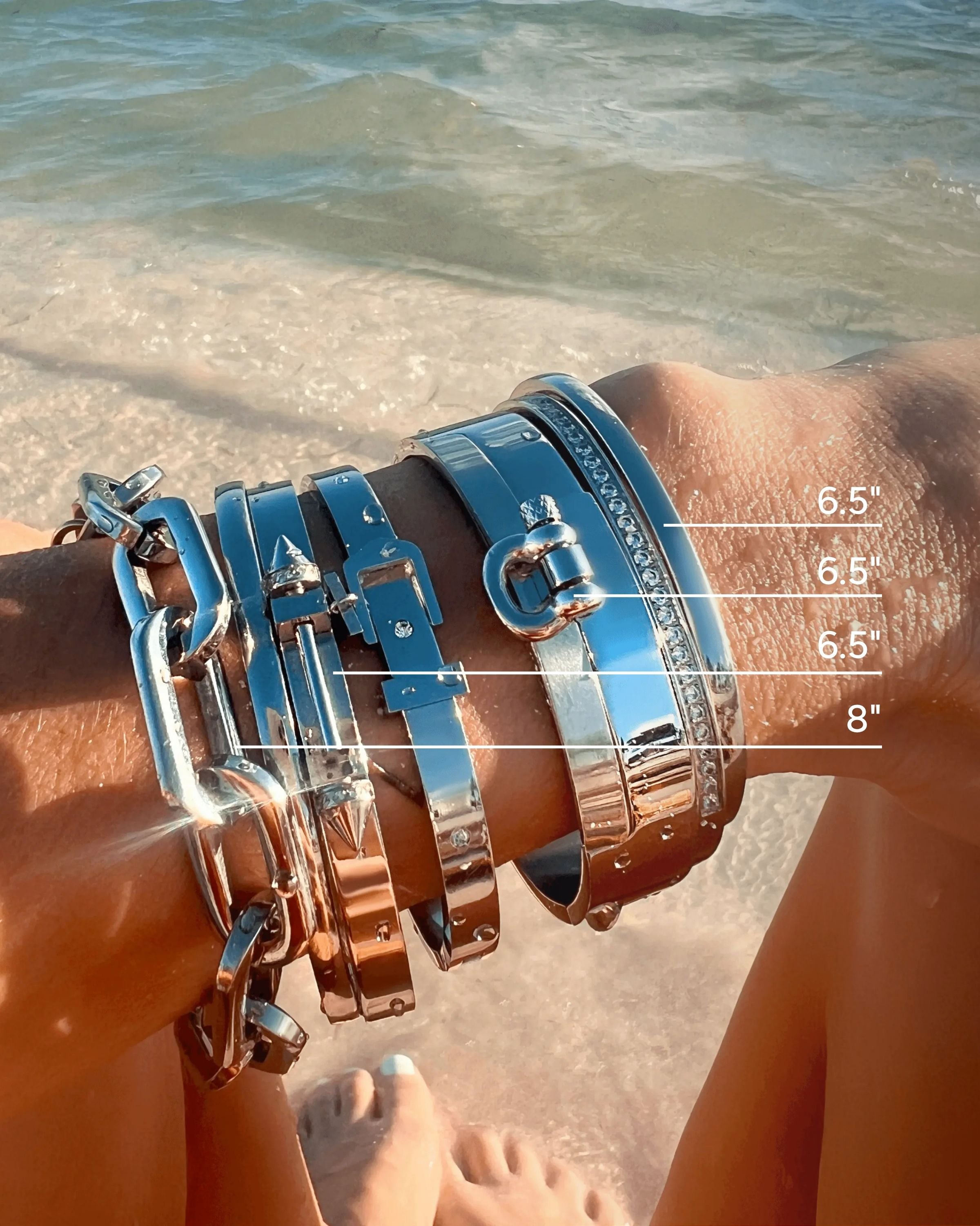 Six-piece silver bracelet stack featuring chunky chain links, sleek bangles, and diamond-accented designs, worn by the beach.