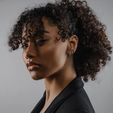 The Tiny Huggies Hoop, a pair of small silver hoop earrings that feature a row of sparkling cubic zirconia stones set in a  pointed, triangular pattern.||| SILVER
