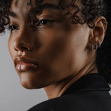 Model wearing The Tiny Huggies Hoop, a pair of small silver hoop earrings that feature a row of sparkling cubic zirconia stones set in a  pointed, triangular pattern.||| SILVER