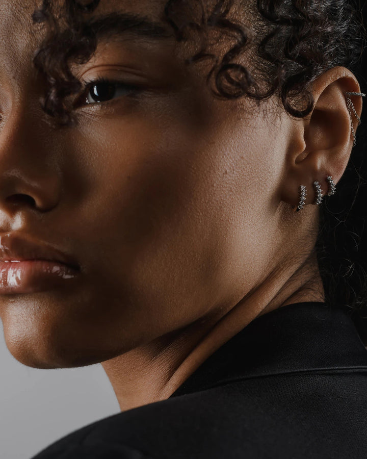 Model wearing the Tiny Huggies Hoop, a pair of small silver hoop earrings that feature a row of sparkling cubic zirconia stones set in a  pointed, triangular pattern. ||| SILVER/5mm