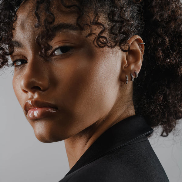 Model wearing the Tiny Huggies Hoop, a pair of small silver hoop earrings that feature a row of sparkling cubic zirconia stones set in a  pointed, triangular pattern.||| SILVER