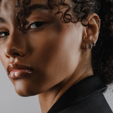 Model wearing the Tiny Huggies Hoop, a pair of small silver hoop earrings that feature a row of sparkling cubic zirconia stones set in a  pointed, triangular pattern. ||| SILVER/5mm