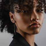 Model wearing the Arrow Earring Chain, a single silver chain earring with a V-shaped arrowhead pendant adorned with sparkling stones and 2 stud earrings. ||| SILVER