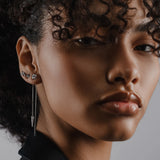 Model wearing the Arrow Earring Chain, a single silver chain earring with a V-shaped arrowhead pendant adorned with sparkling stones and2 stud earrings. ||| SILVER