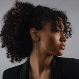 Model wearing the Arrow Earring Chain, a single silver chain earring with a V-shaped arrowhead pendant adorned with sparkling stones and2 stud earrings. ||| SILVER