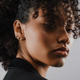 Model wearing 3 Tiny Huggies Hoop that are small gold hoop earrings that feature a row of sparkling cubic zirconia stones set in a  pointed, triangular pattern.||| GOLD