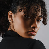 Model wearing the Endless Diamond Earring Chain, a gold chain featuring seven bezel-set diamond-like stones. She is also earing a tiny lightning stud earring