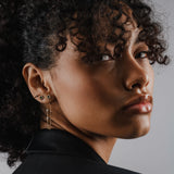 Model wearing the Endless Diamond Earring Chain, a gold chain featuring seven bezel-set diamond-like stones. She is also earing a tiny lightning stud earring