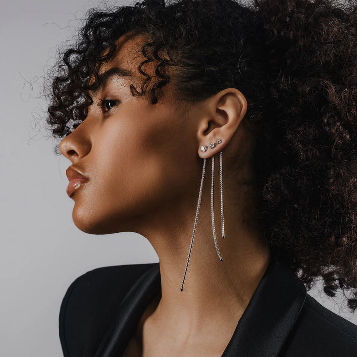 Model wearing three Tennis Earring Chains, a single long silver chain earring with tiny sparkling stones.||| SILVER