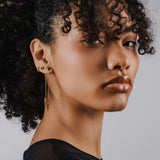 Model wearing the Arrow Earring Chain, a single gold chain earring with a V-shaped arrowhead pendant adorned with sparkling stones and 2 stud earrings.||| GOLD