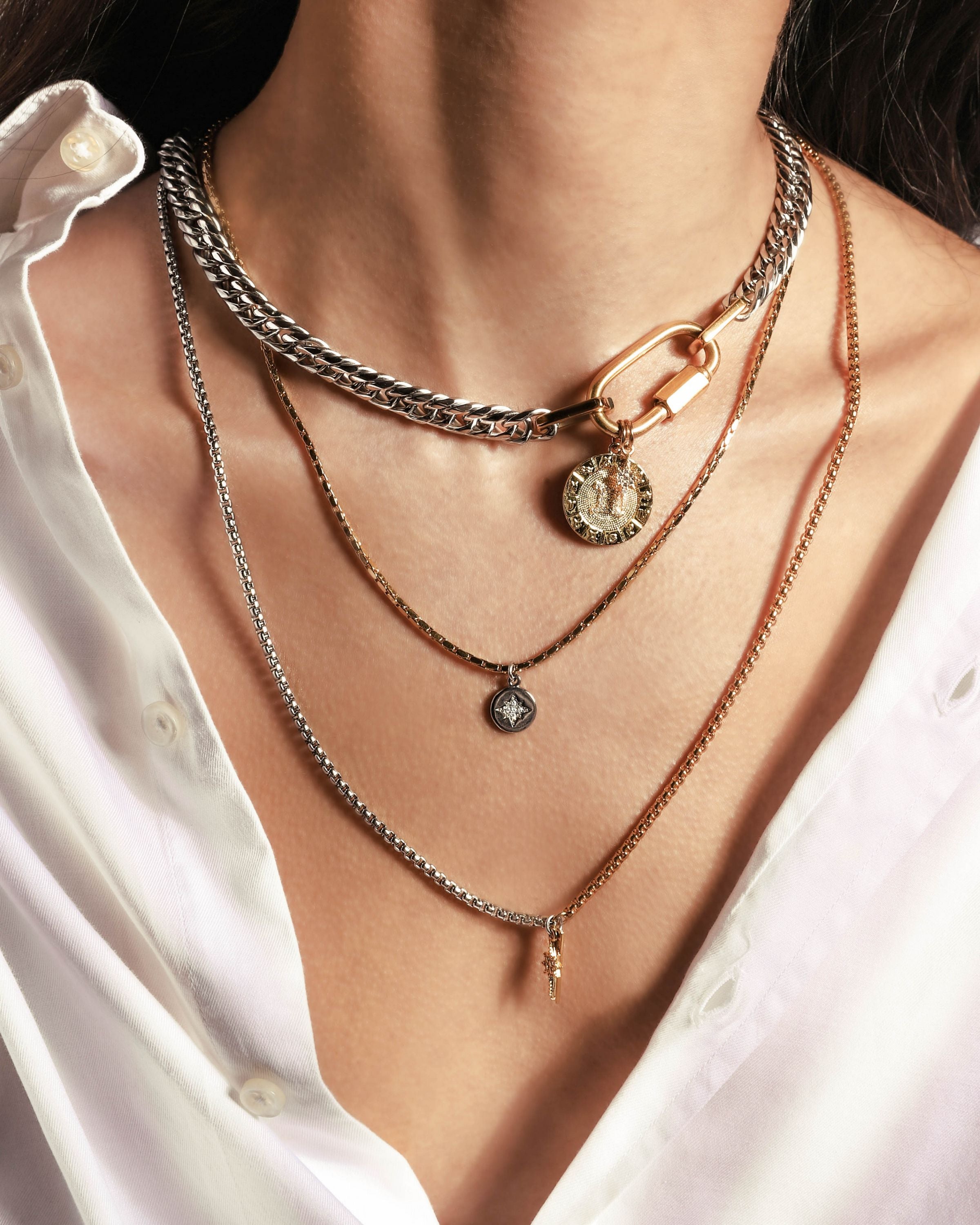 Model wearing the Anne Zodiac Necklace which is a three pieces layered necklace set. Includes one silver chain with 18k gold plated carabiner and Gold Filled CAPRICORN Zodiac with Micro Pave Constellation charm, thin gold necklace with silver circle charm and another long necklace in half gold and silver with spike shaped charm and Gold Plated Micro Pave Studded Star. |||