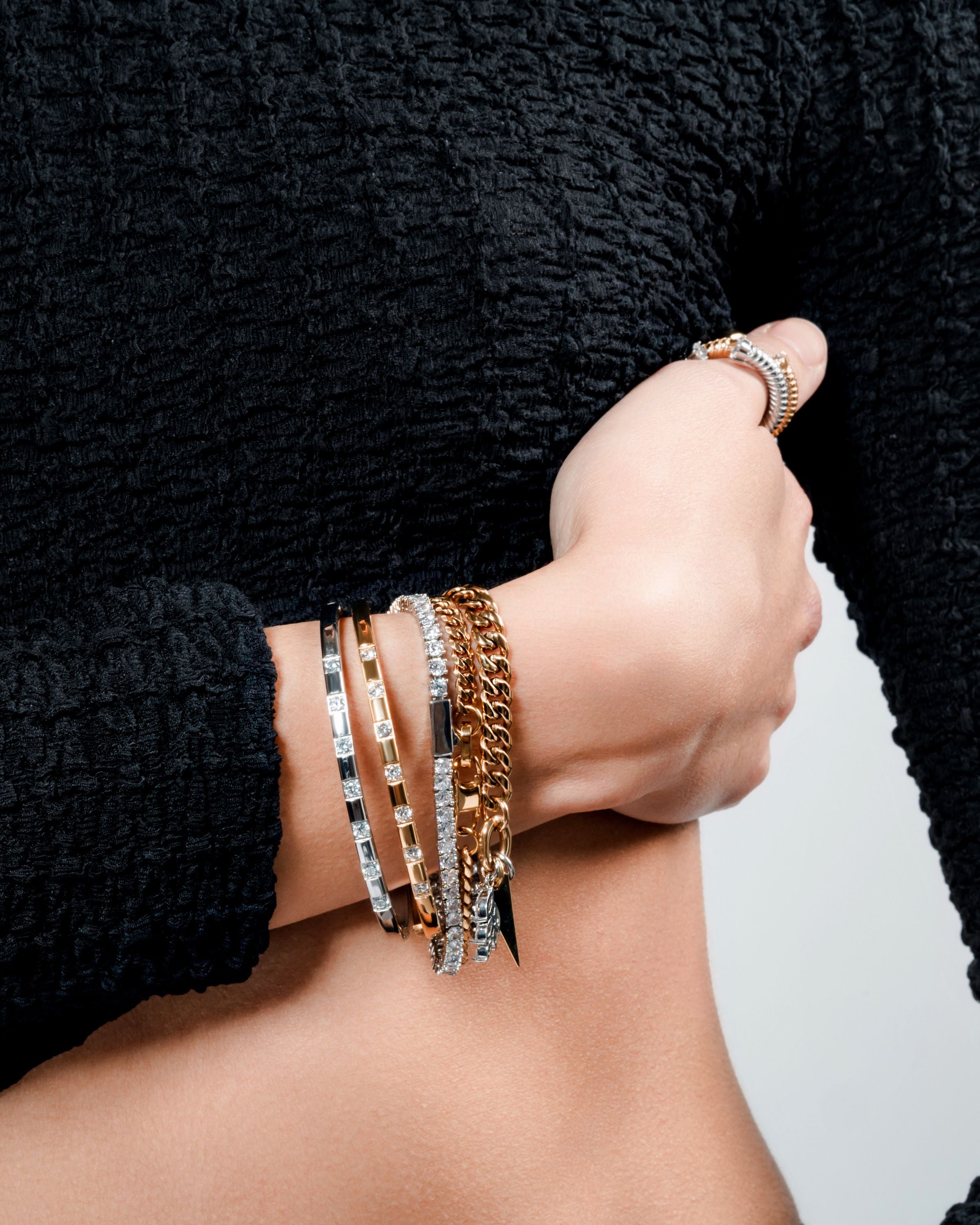 Model wearing a mixed metal bracelet stack with gold and silver bangles, a tennis bracelet, and a chunky chain bracelet on the wrist