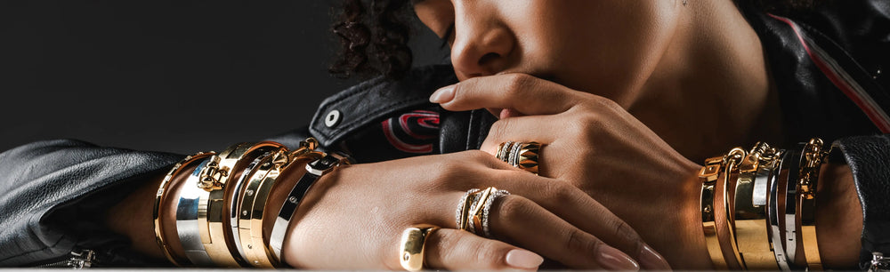 "Model wearing a bold mix of multiple Artizan Joyeria jewelry pieces, including stacked gold and silver bangles and intricately designed rings, styled against a black leather jacket for a modern, edgy look."