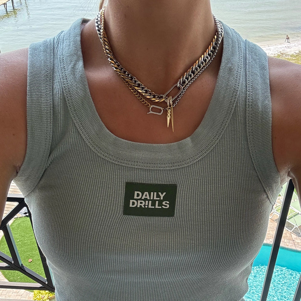 A close-up of layered gold and silver chain necklaces styled over a casual green tank top with 