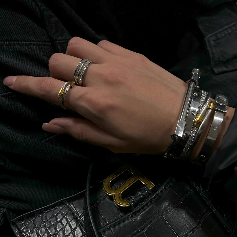 Close-up of a hand in dark attire showcasing an array of stacked bracelets and rings with a luxury brand clutch in the background.