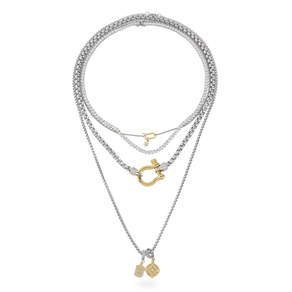 The Herradura Signature Charmed Tennis Set, which is a three-piece layered silver necklace set, features intricate tennis chains with shimmering stones and gold accents, including a bold clasp and two elegant gold charms for a statement-making yet refined style.