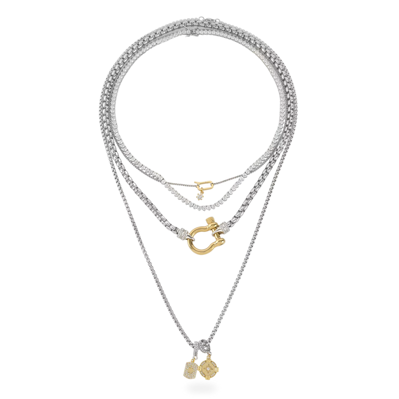 The Herradura Signature Charmed Tennis Set, which is a three-piece layered silver necklace set, features intricate tennis chains with shimmering stones and gold accents, including a bold clasp and two elegant gold charms for a statement-making yet refined style.