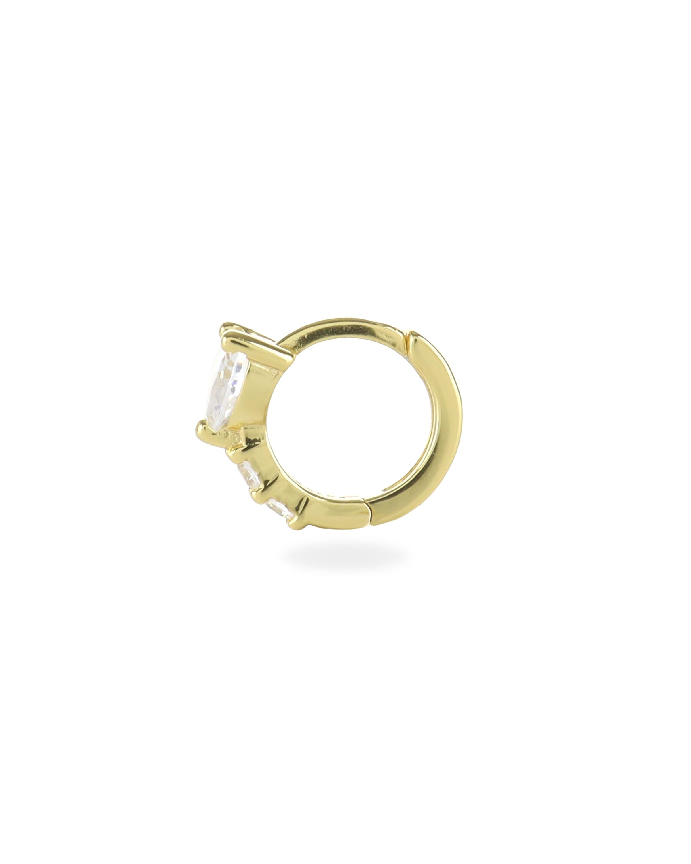 The One Stone Gold Piercing Hoops, which is a gold hoop earring, feature a central heart-shaped stone with additional sparkling accents along the band.