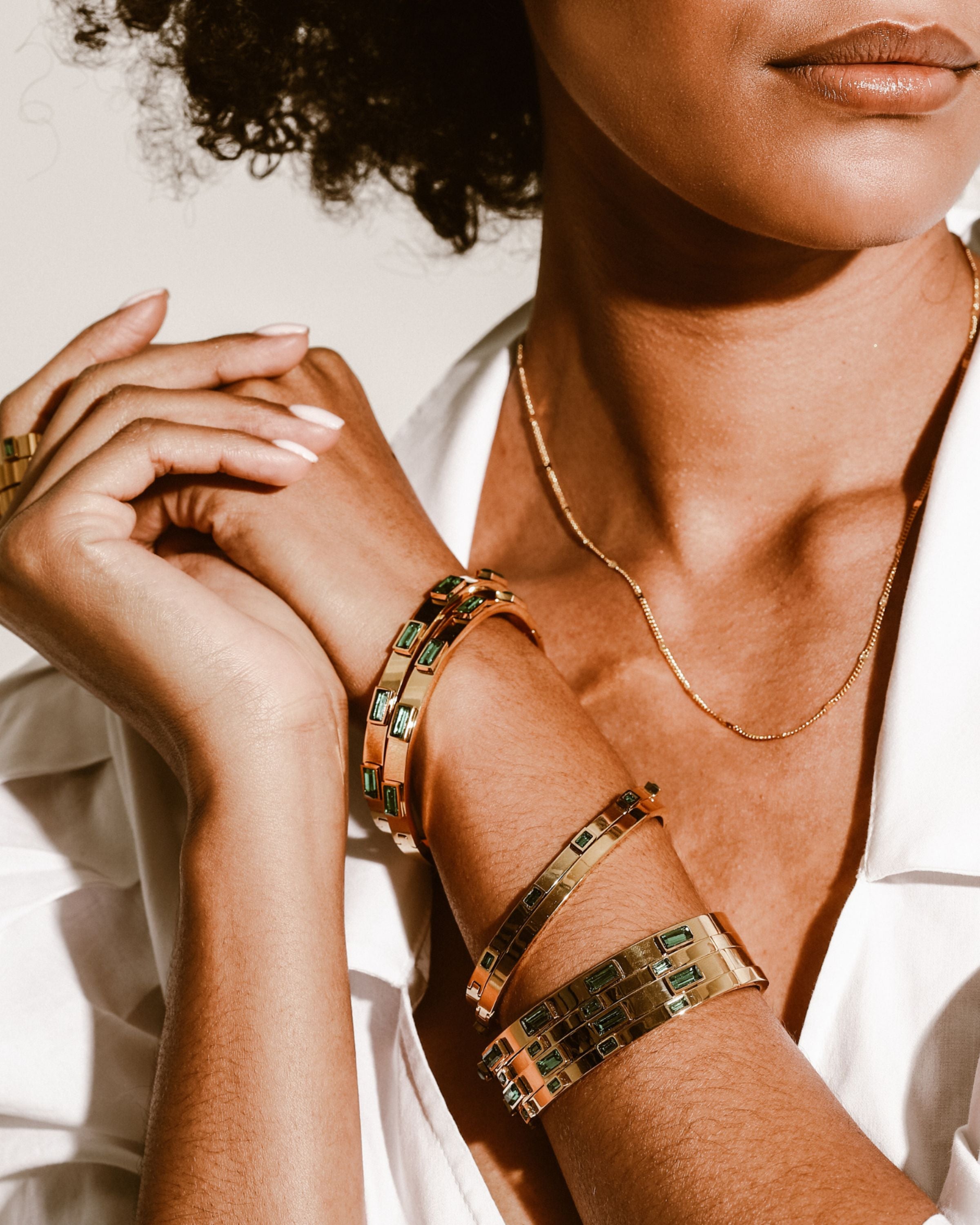 Model wearing a stack of Emerald Bangle and Emerald thin bangles. She is wearing three emerald rings and also a thin chain gold necklace.