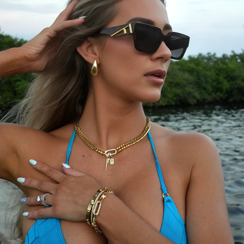 A woman in a blue bikini, wearing black sunglasses and gold jewelry from artizan joyeria