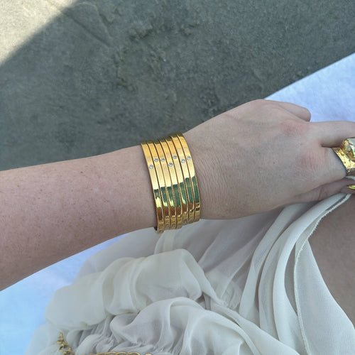 The bracelet in the image appears to be a stack of gold bangles with diamonds. The bangles are all the same width and have a similar design, with a single diamond set in the center of each bangle. The diamonds are all the same size and appear to be white.