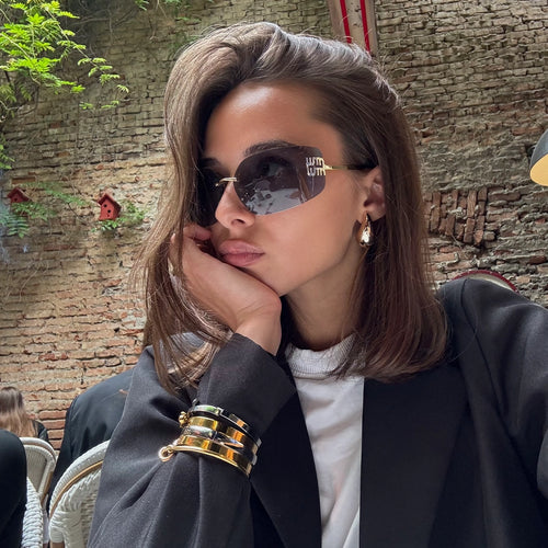 A woman in a restaurant wearing black see through glasses,  whit a black blazer and a white shirt, with a bangle stack of mix metals from artizan joyeria