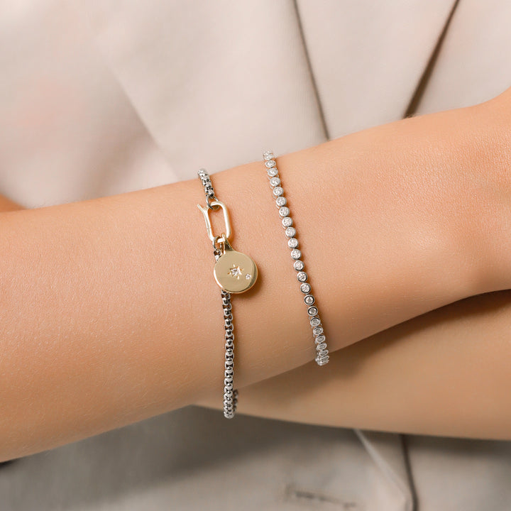 Model wearing the Tennis and the Box Bracelet Set, a two-piece silver bracelet set featuring a diamond-like tennis bracelet and a box chain bracelet with a gold north star charm accented with diamond-like stones.