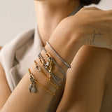 Model wearing layered can opener bracelets including the Can Opener Chain Bracelet featuring a gold Cuban chain, a silver circle charm with sparkling diamonds, and a star-shaped link charm. 