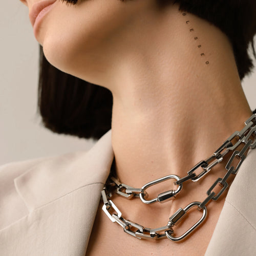 Model  wearing two Carabiner Square Puerto Necklaces, which is a silver chain necklace featuring a unique silver carabiner clasp.