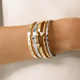 Model wearing  the Triangle Stack, a five-piece bangle set featuring gold and silver bangles with cubic zirconia accents and a triangle clasp detail.