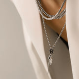 Model wearing The Needle and the Tennis Necklace Set, a three-piece silver necklace set featuring two chains, a diamond-like tennis necklace, and a dangling spike charm.
