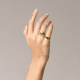 Model wearing the Madness Ring Stack, a three-piece gold and silver ring stack featuring a gold pinky ring with a single diamond-like stone, a silver ring with diamond-like accents, and a gold ring with a textured geometric design.