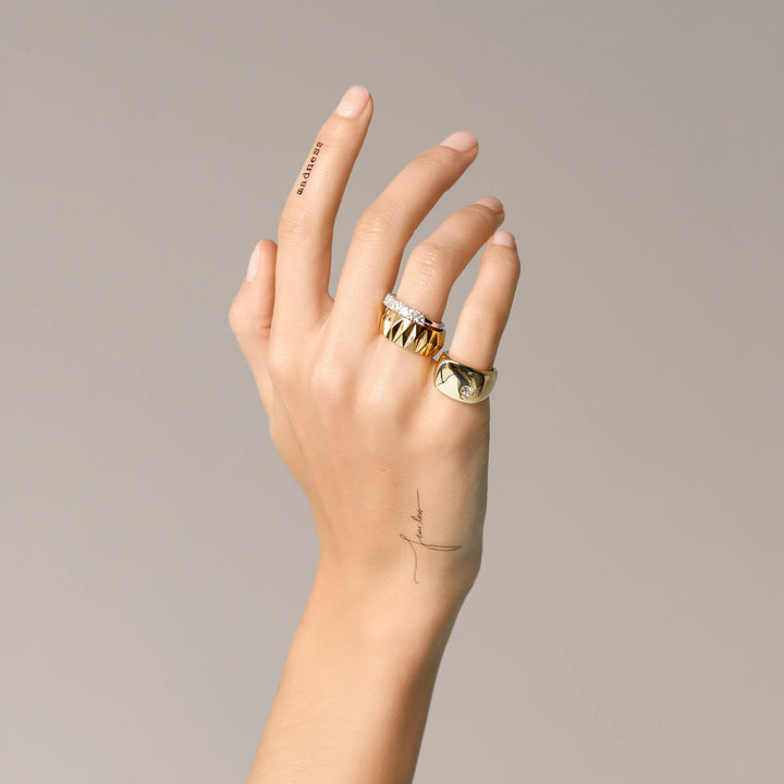Model wearing the Madness Ring Stack, a three-piece gold and silver ring stack featuring a gold pinky ring with a single diamond-like stone, a silver ring with diamond-like accents, and a gold ring with a textured geometric design.