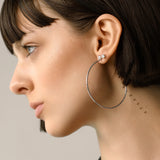 Model wearing The Solitaire Hoop, a pair of silver hoop earrings, with two diamond-like stone studs.