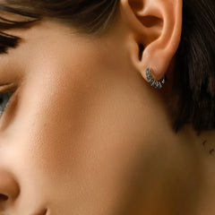 Model wearing the Prong Emerald Hoops, a pair of silver hoop earrings featuring prong-set emerald accents.