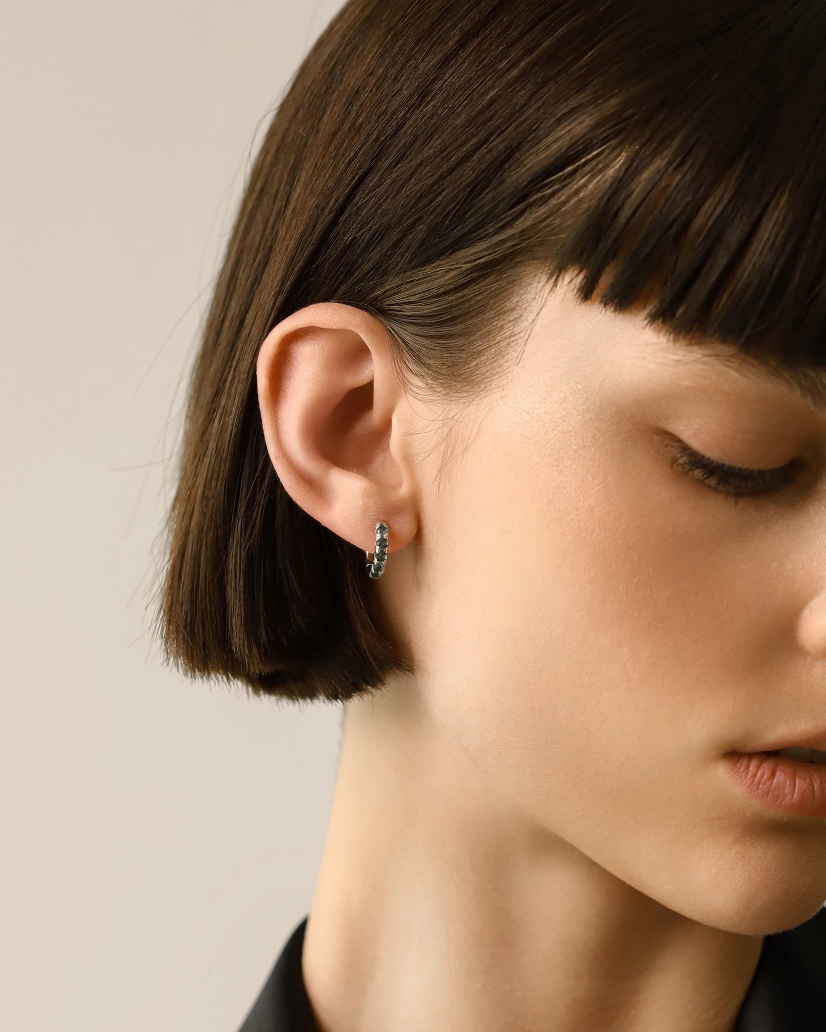 Model wearing one Eternity Emerald Hoops, a silver hoop featuring emerald accents.