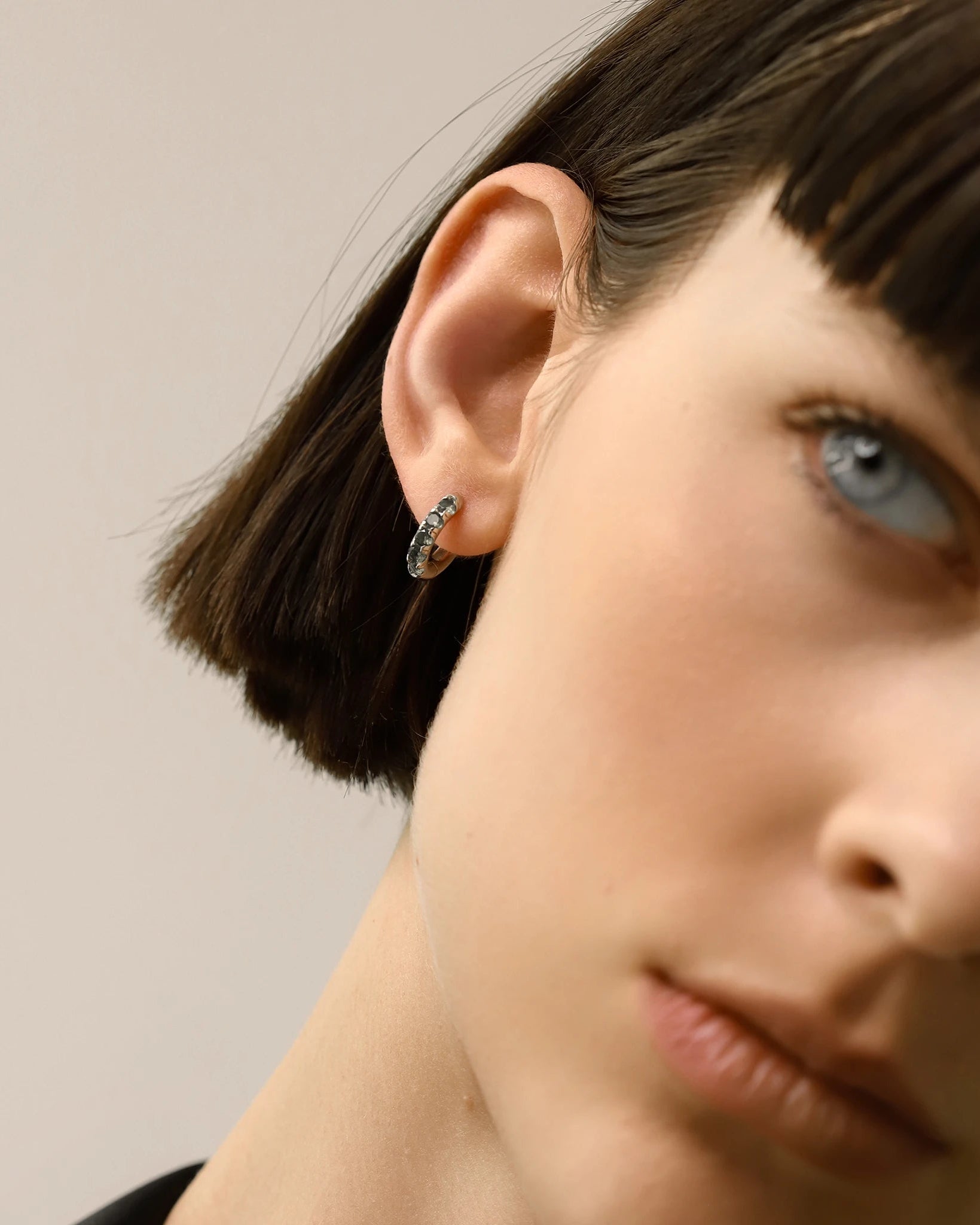 Model wearing one Eternity Emerald Hoops, a silver hoop featuring emerald accents.