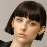 Model wearing the Prong Emerald Hoops, a pair of silver hoop earrings featuring prong-set emerald accents.