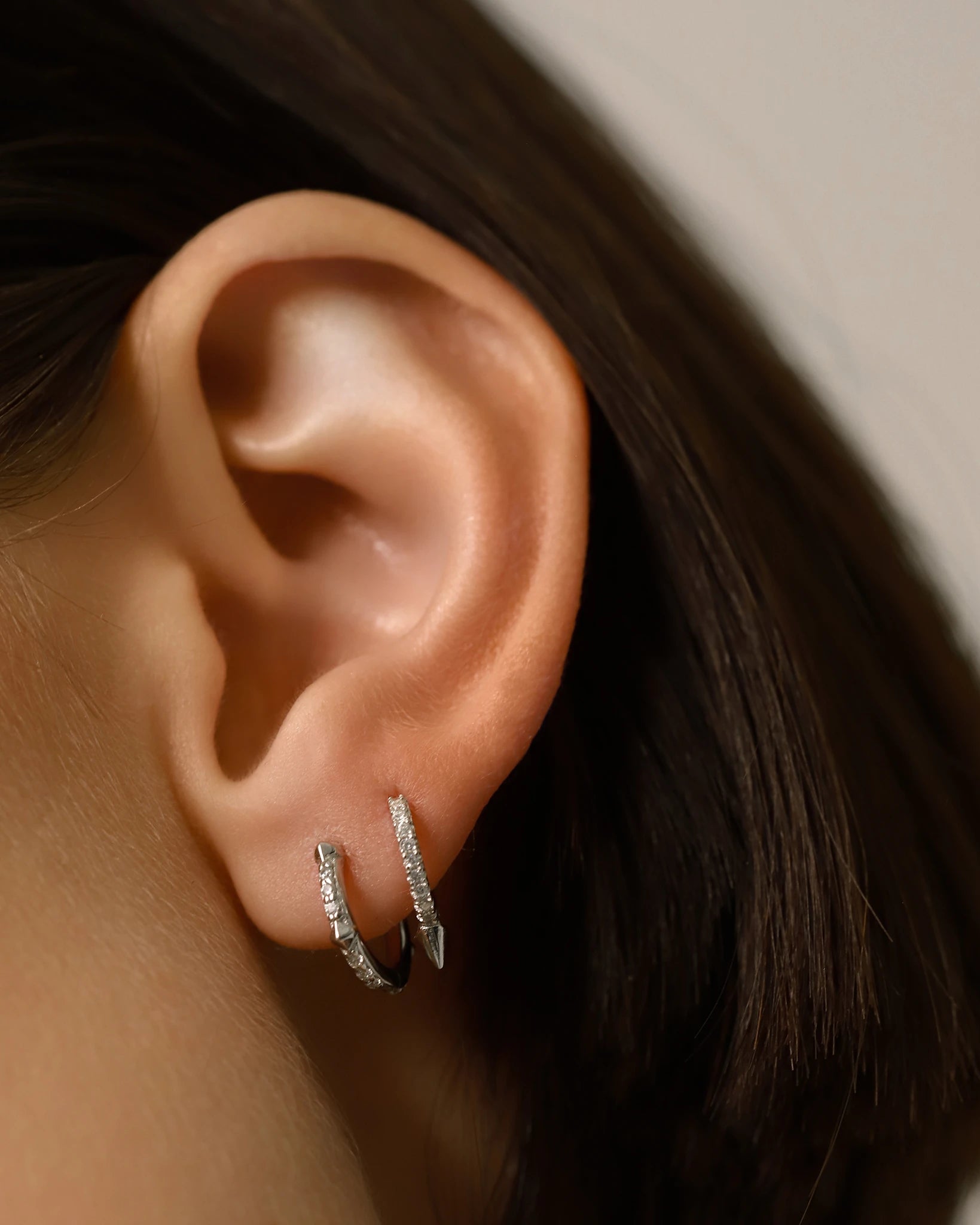 The MINI SHOT HOOP, which is a pair of elegant silver earrings, showcases a minimalist hoop design encrusted with shimmering cubic zirconia stones and finished with a sleek pointed charm for a modern and edgy touch. Perfect for enhancing any outfit with a subtle yet sophisticated sparkle.