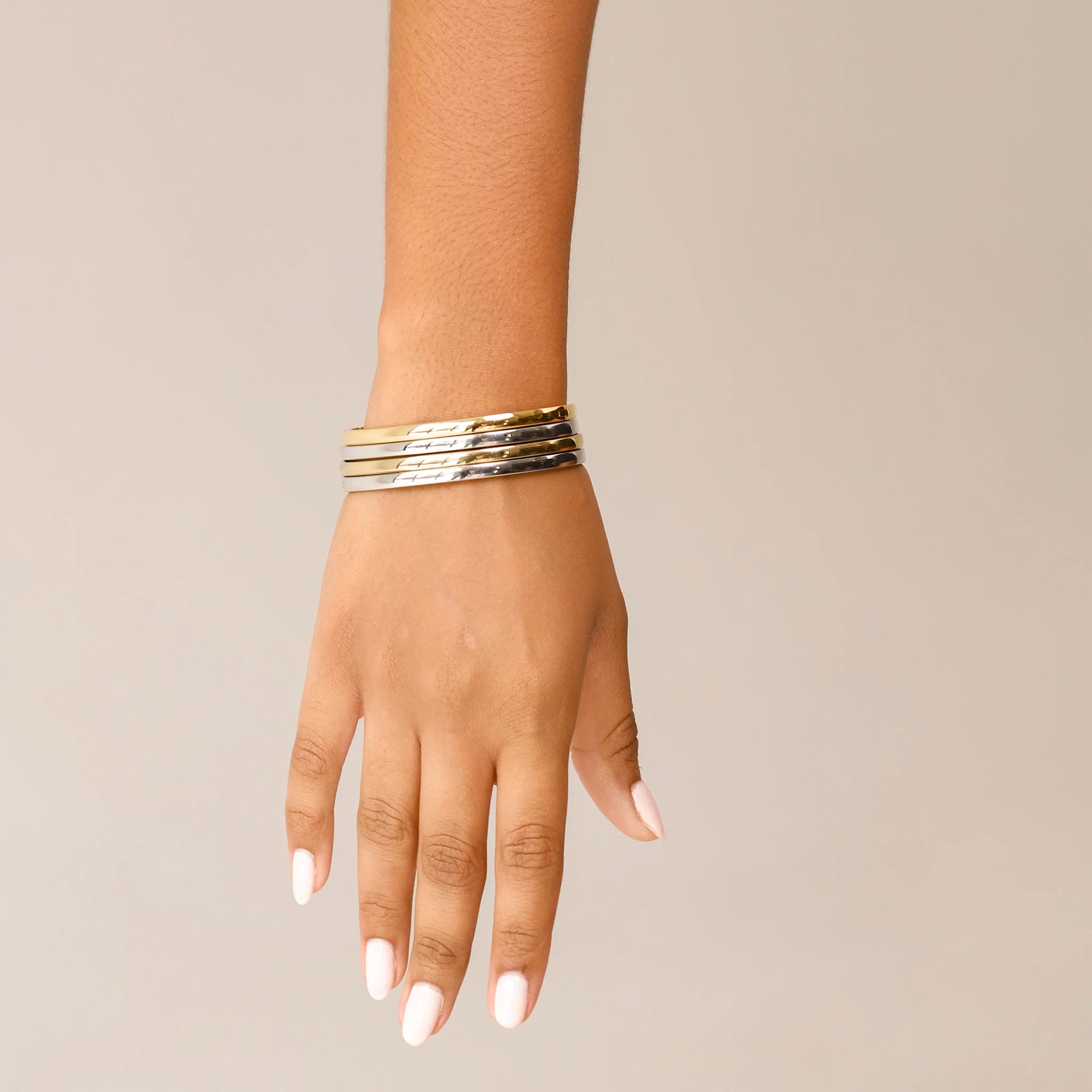 The Plain Thin Set, which is a four-piece bracelet stack, features alternating gold and silver bands with a sleek and polished finish, offering a minimalist yet sophisticated look for versatile styling.