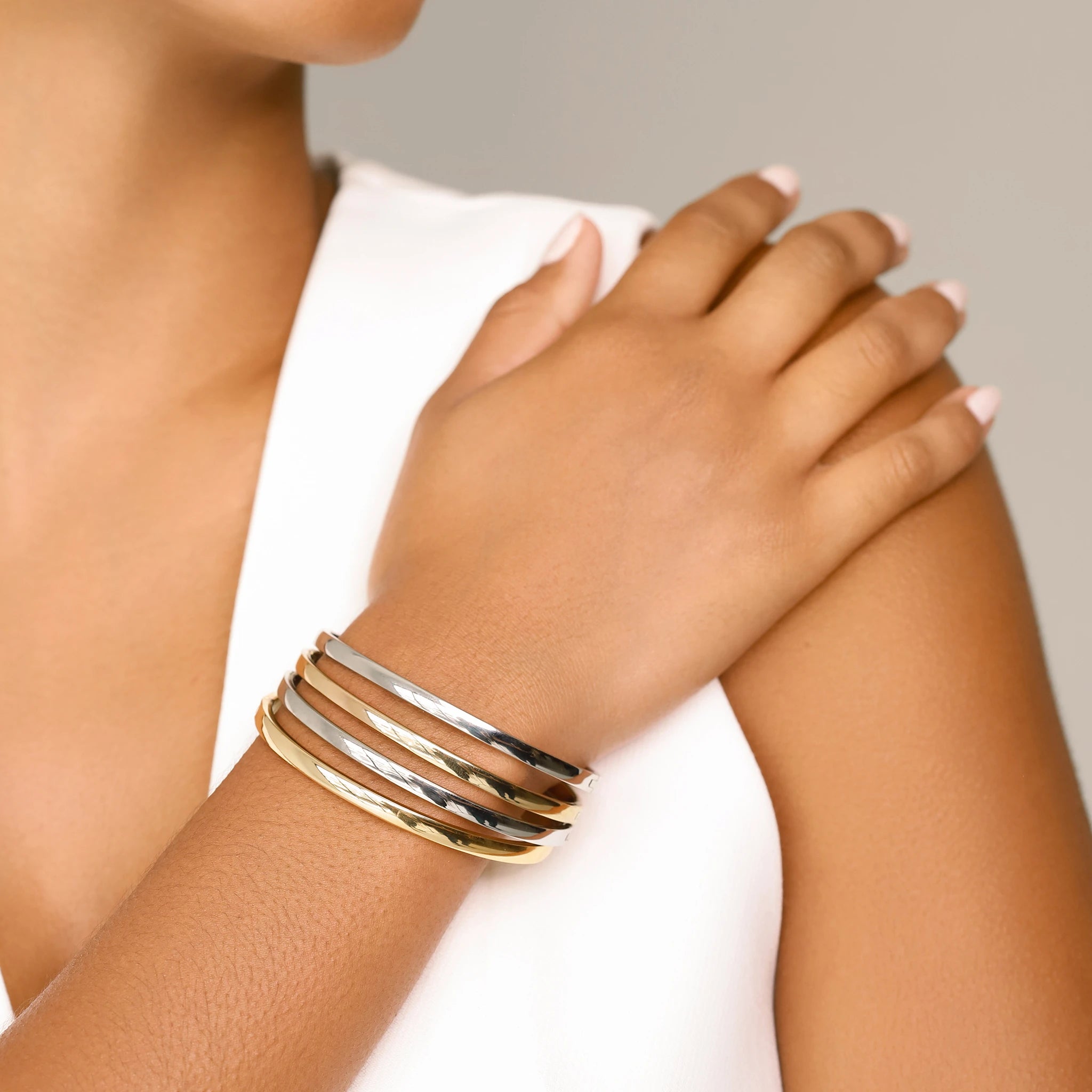 The Plain Thin Set, which is a four-piece bracelet stack, features alternating gold and silver bands with a sleek and polished finish, offering a minimalist yet sophisticated look for versatile styling.
