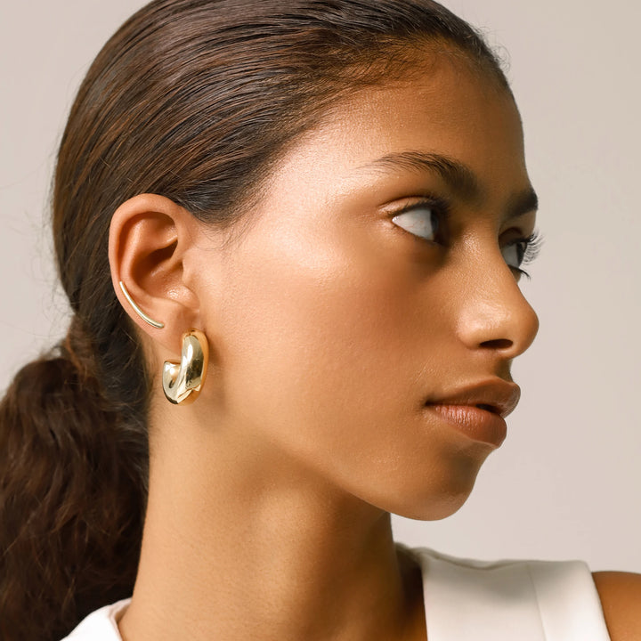 Model wearing the Bagel Hoop, a pair of chunky gold hoop earrings with a rounded, torus shape and a long plain climber earring.