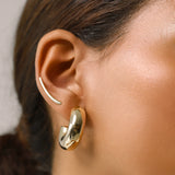 Model wearing the Bagel Hoop, a pair of chunky gold hoop earrings with a rounded, torus shape and a long plain climber earring.