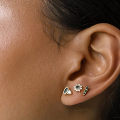 The Emerald Oval Stud Earring, shown as part of a gold ear stack alongside two other complementary studs, features a marquise-cut green emerald and a small round crystal. This chic and versatile piece adds a refined touch to a layered ear look, enhancing any outfit with a hint of color and sparkle."