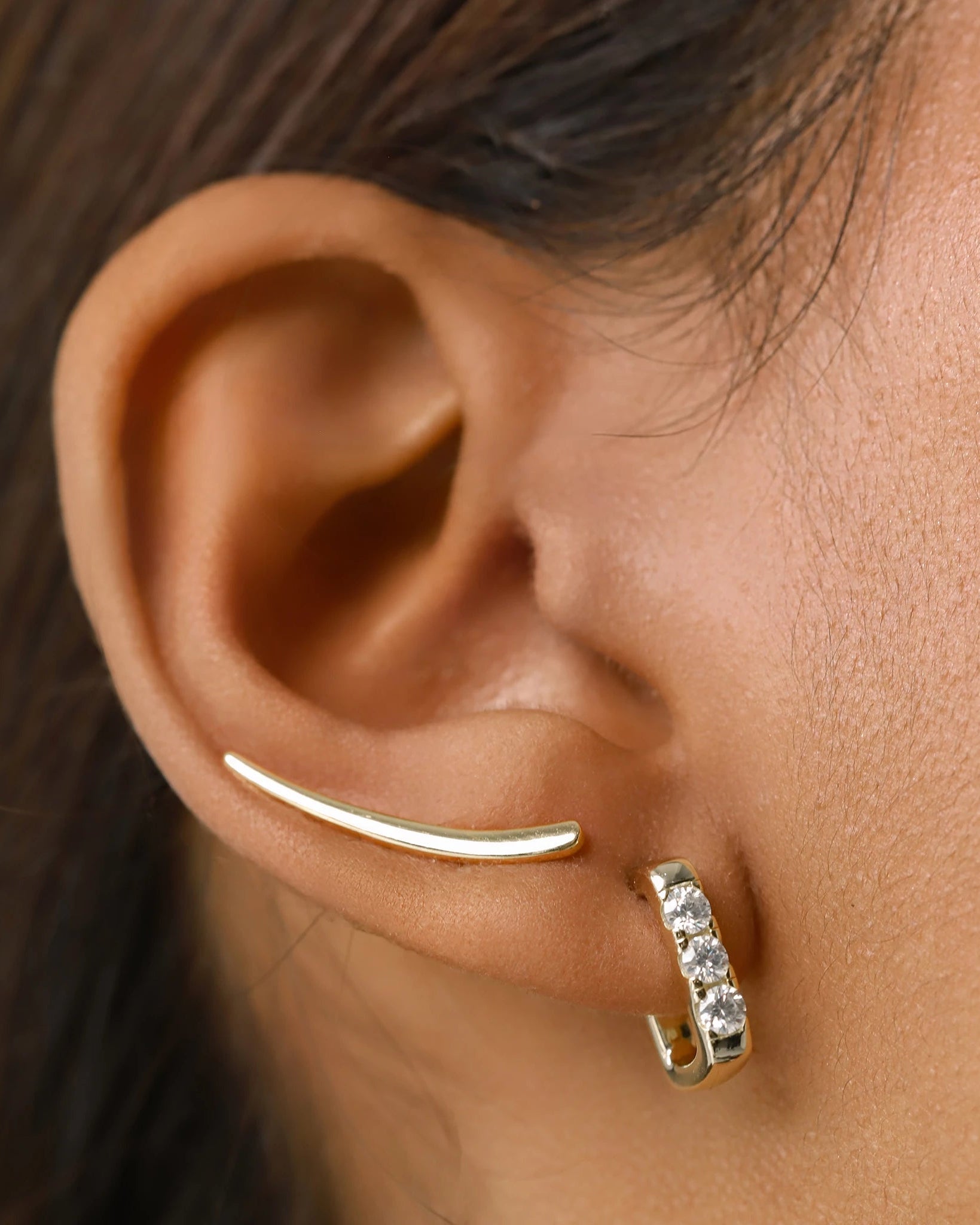 The RECTANGLE HOOP, which is a single elegant gold-tone earring, features a sleek rectangular hoop design with sparkling cubic zirconia accents. This modern yet minimalist piece adds a touch of sophistication to any outfit, perfect for layering with other earrings or wearing alone for a statement look.